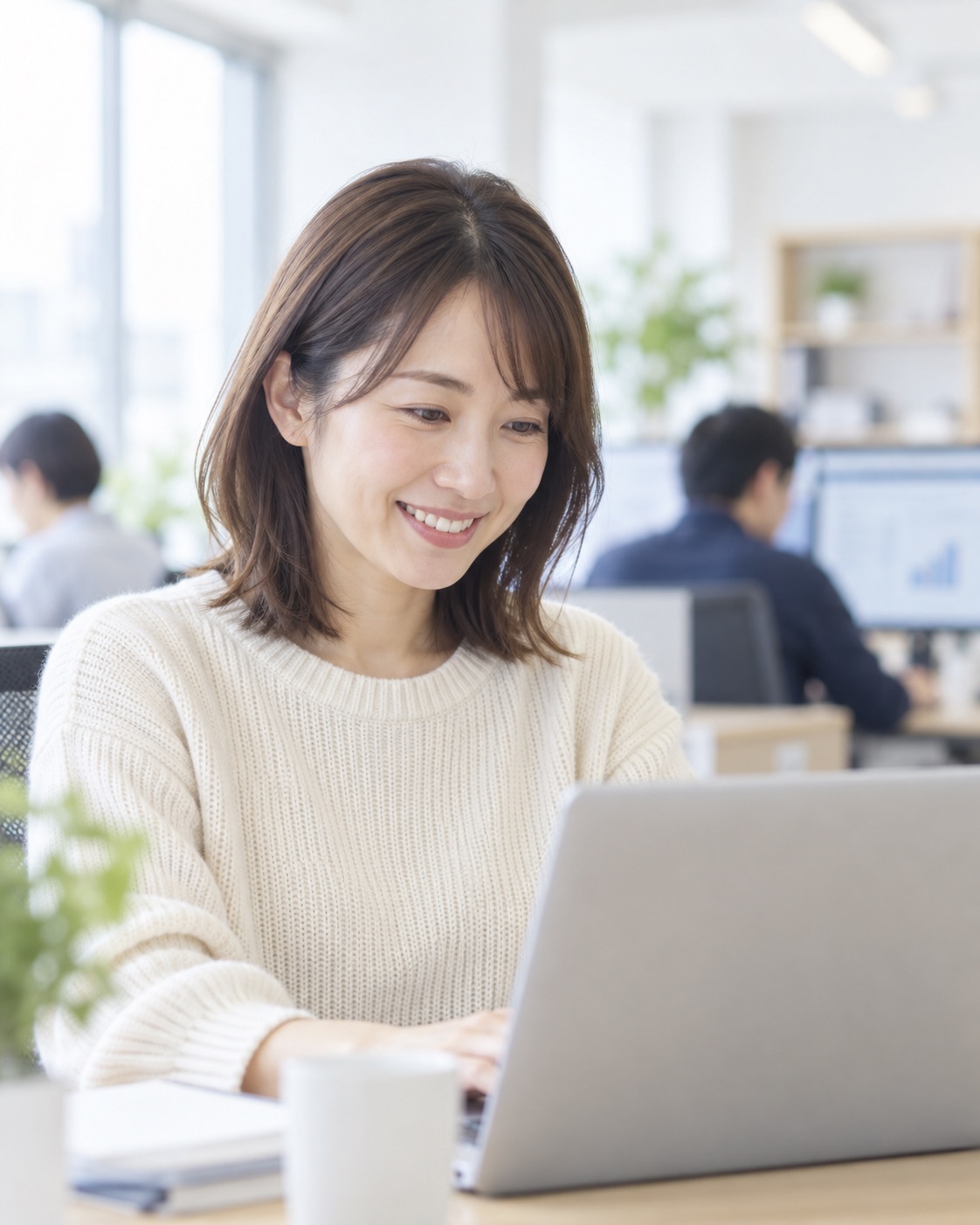 明るいオフィスでノートパソコンを見て笑顔になる女性