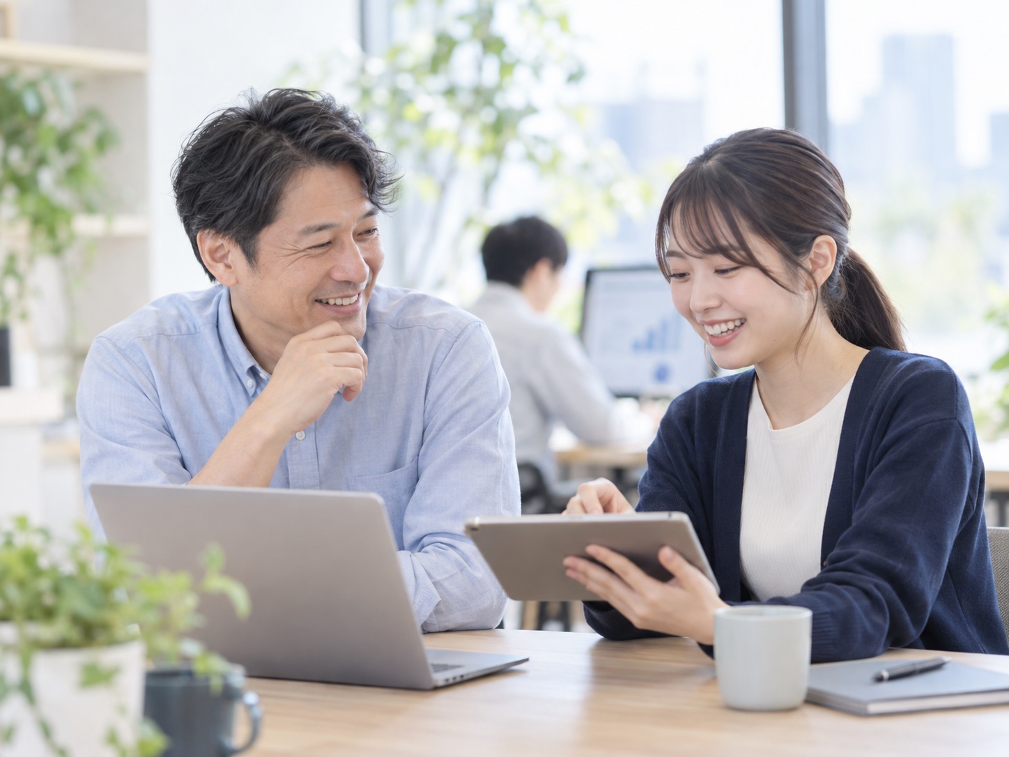 窓際の打ち合わせスペースでタブレットを見ながら話す2人